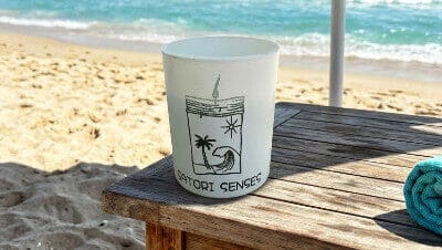 Vela aromática de playa tropical de cera de soja en una mesita de playa junto al mar